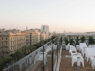 Rooftop terrace view overlooking the urban landscape at dusk in Bari, Italy, with outdoor furniture set against the city skyline